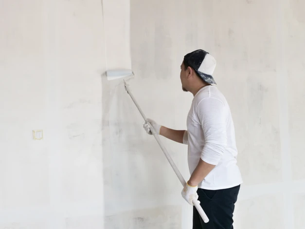 Peintre professionnel appliquant une peinture blanche sur un mur intérieur à l'aide d'un rouleau à peinture