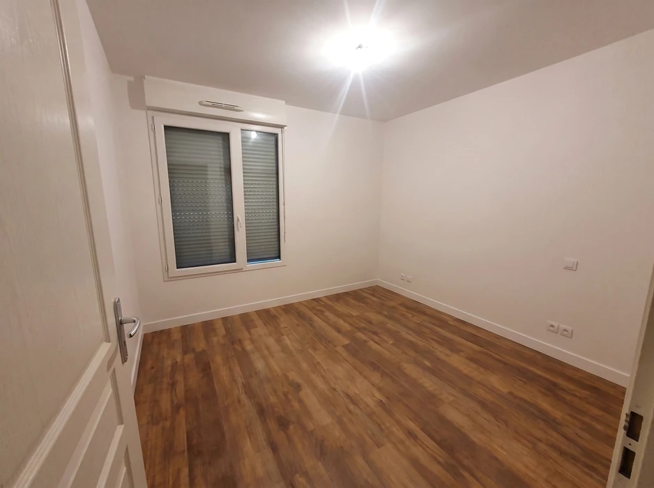 Chambre vide, lumineuse, murs blancs, parquet stratifié ton chêne foncé