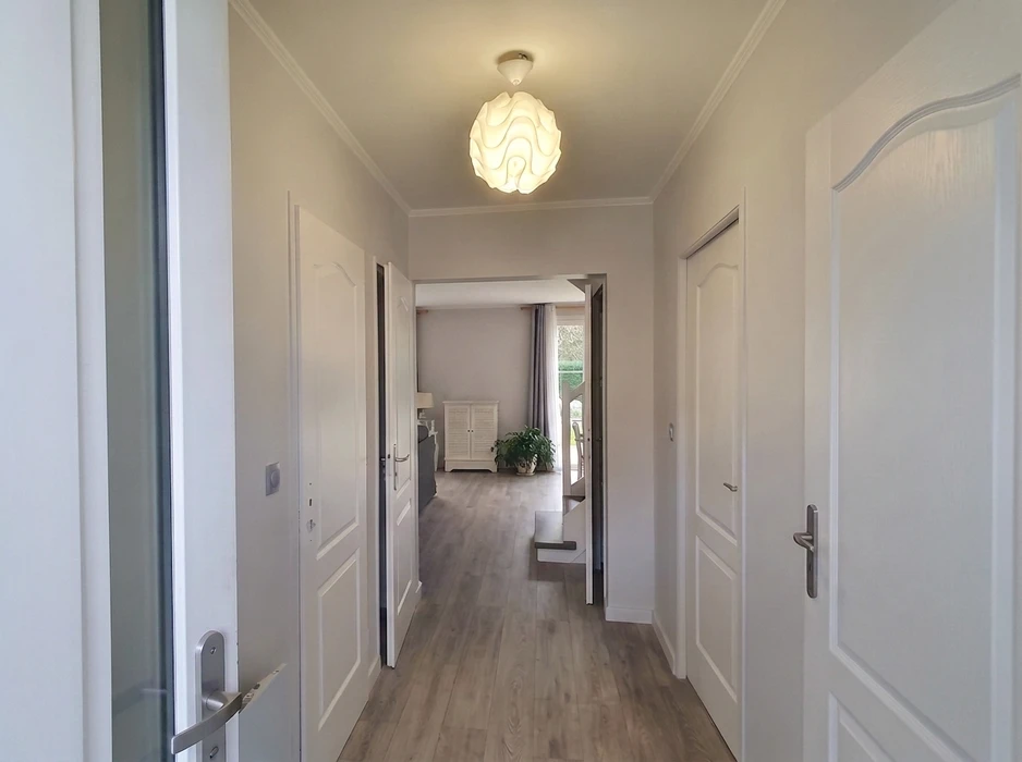 Couloir d'entrée lumineux d'un appartement moderne, menant vers un séjour avec baie vitrée